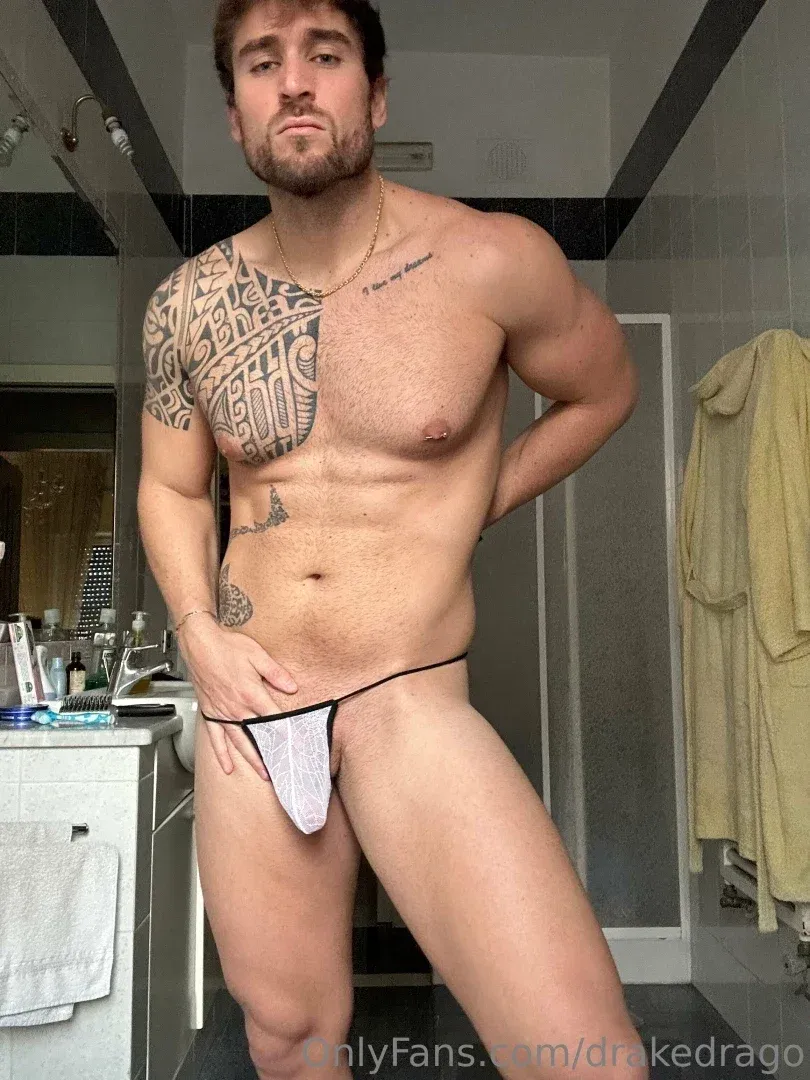 Drake dans une salle de bain portant un string gris et une chaîne dorée, montrant des tatouages sur le torse.