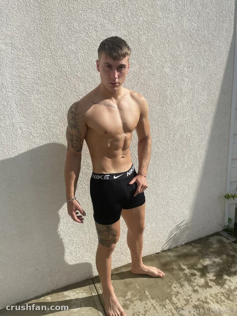 Creador sin camiseta con boxers negros de pie frente a una pared blanca bajo la luz del sol