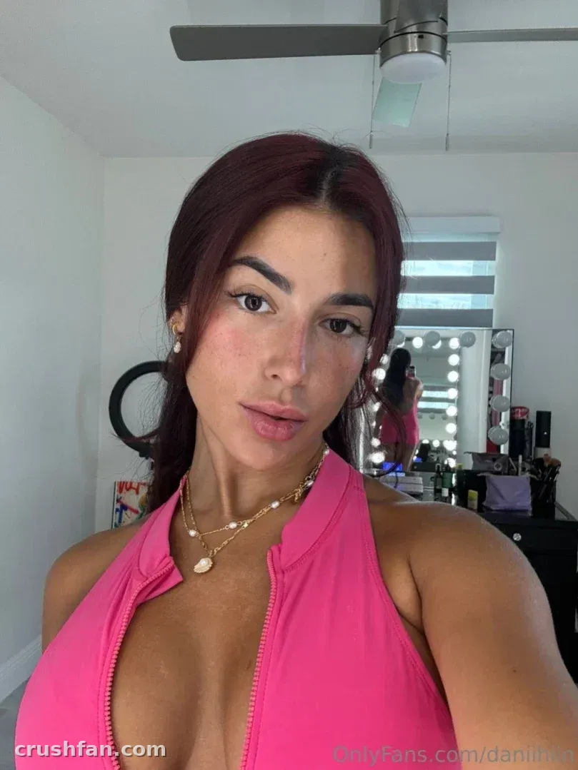 Dani ♥️ in a pink halter top posing in front of a lit vanity mirror.