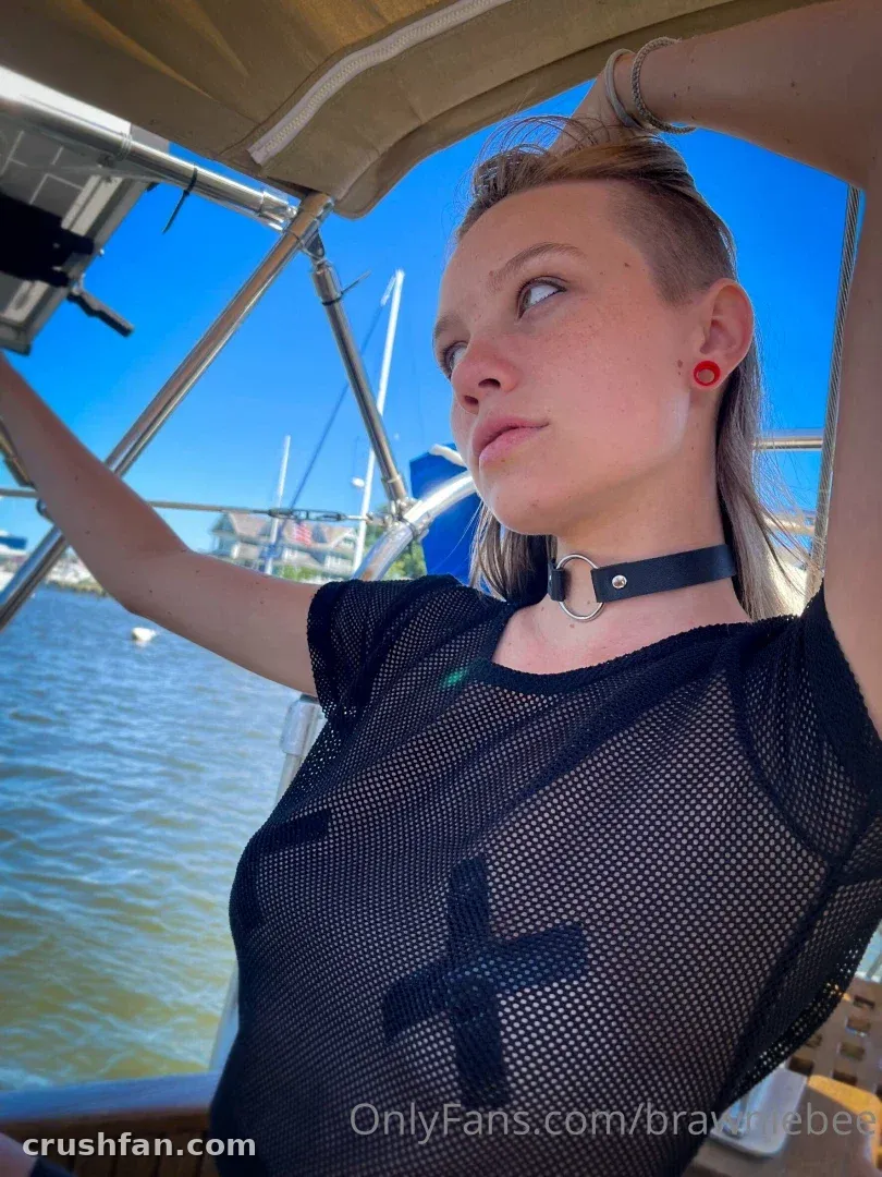 Brawniebee on a boat in a black mesh top and choker under a blue sky