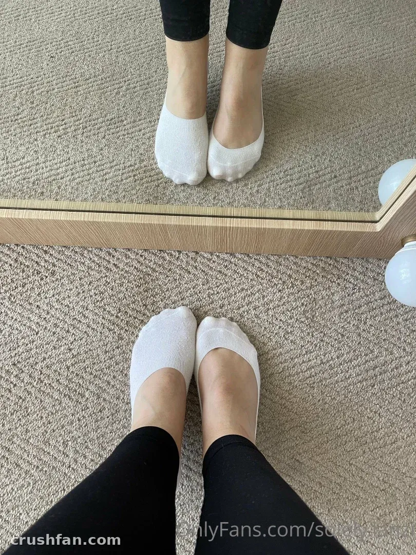 Lanzi in weißen Wollsocken und schwarzen Leggings, auf beigem Teppich neben einem Standspiegel stehend.