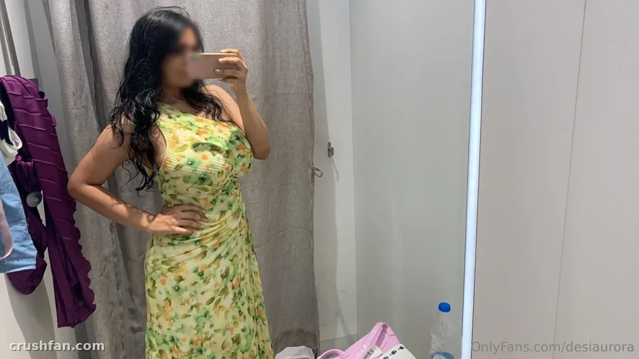 Desi Aurora in a green floral dress taking a mirror selfie in a bright room