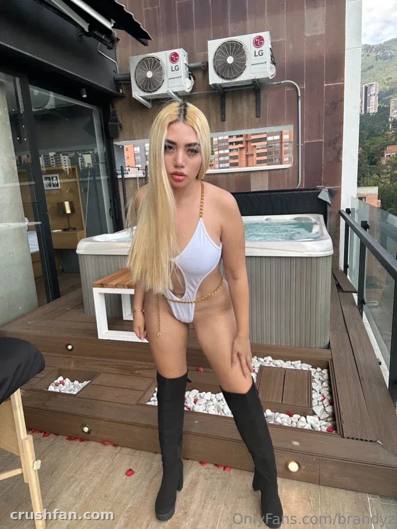 Creator in a white cut-out swimsuit and black boots on a rooftop deck with a hot tub