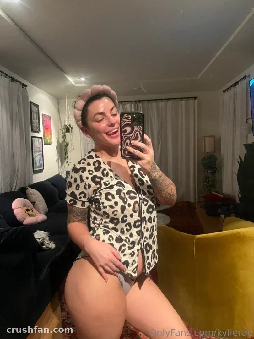 Kylie Rae in a leopard print top taking a mirror selfie in a living room.
