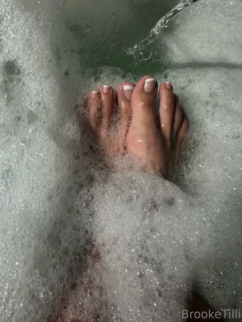 Pieds aux ongles peints d'un ton pâle reposant parmi une épaisse mousse de bain blanche
