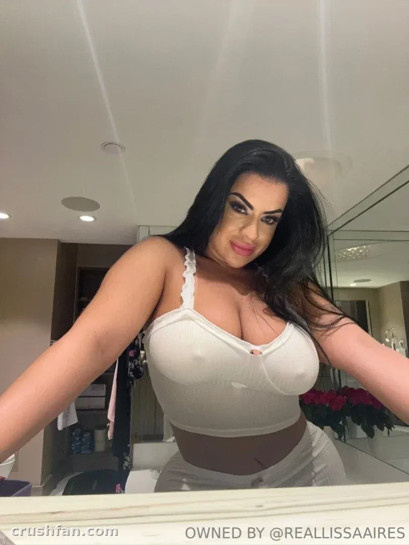 Lissa Aires in a white lace-trim crop top taking a mirror selfie indoors