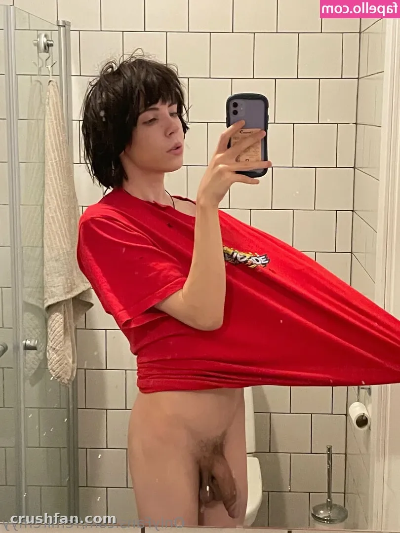 Remi in a red t-shirt taking a mirror selfie in a tiled bathroom