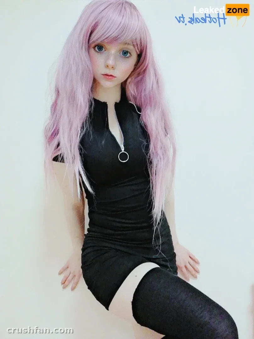 Creator con largo pelo rosa, vestido negro y medias hasta el muslo sobre un fondo blanco.