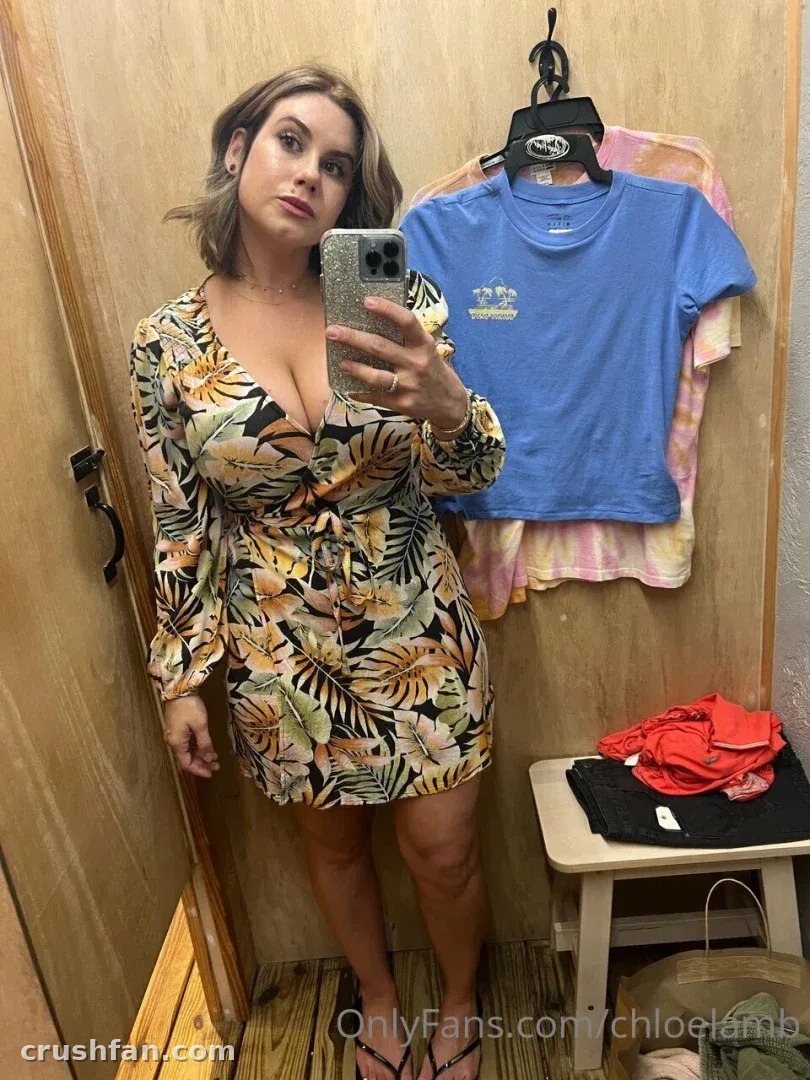 Chloe Lamb in a tropical print dress taking a mirror selfie in a fitting room.