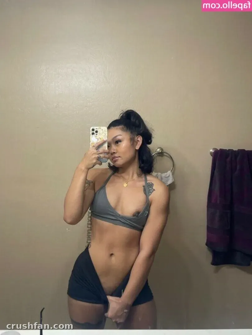 Creator in a grey halter top and dark shorts taking a mirror selfie against a beige wall