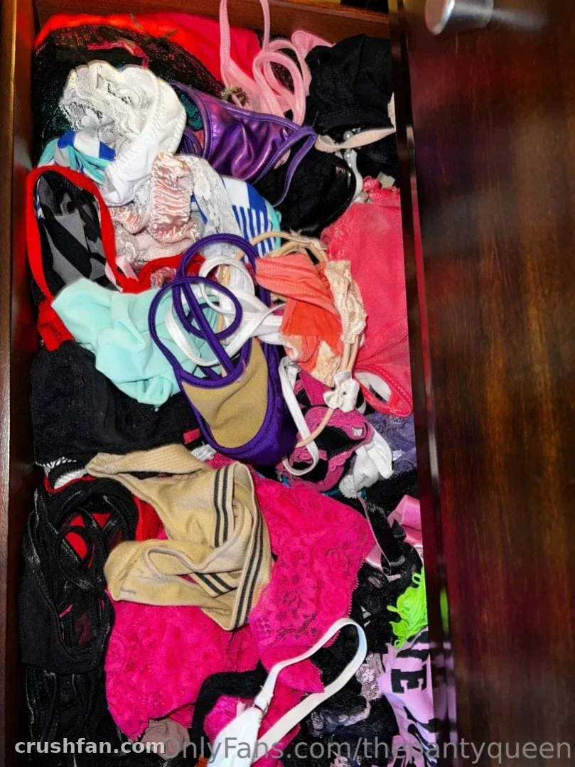 Gaveta de madeira aberta cheia de lingerie e meias coloridas em rosa, preto e roxo.