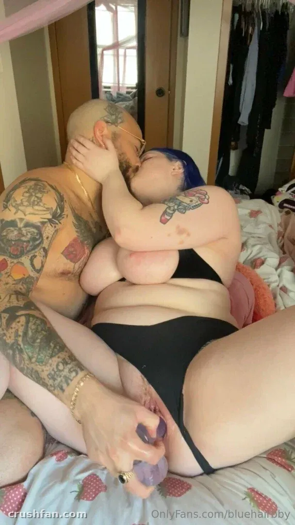 Blue in schwarzer Unterwäsche, die einen engen Moment mit einem tätowierten Partner auf einem Bett in einem Schlafzimmer teilt.