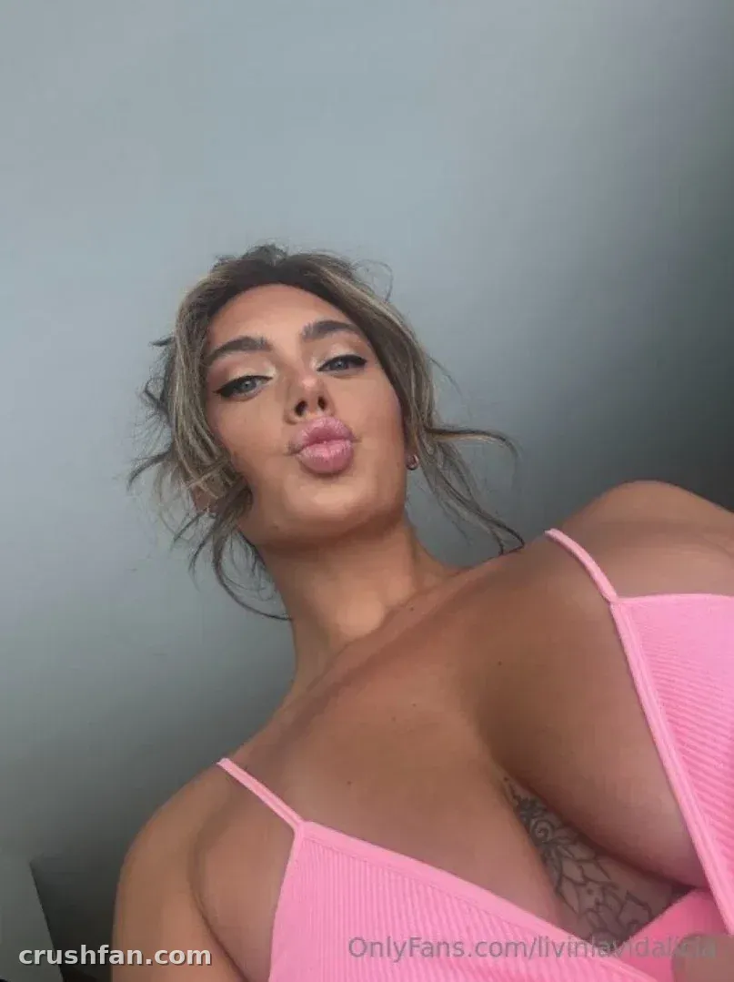 Alicia in a pink ribbed top making a playful face against a grey wall