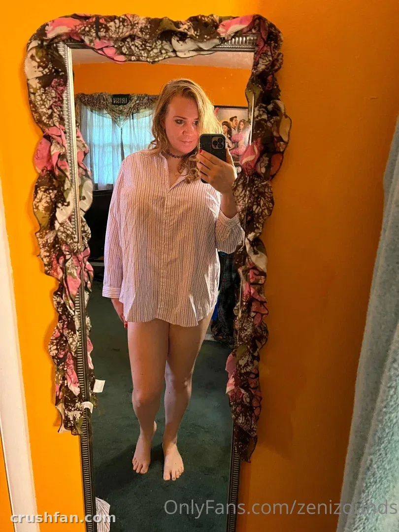 Creator Zeni Zounds takes a mirror selfie in a striped shirt in a warm orange room.