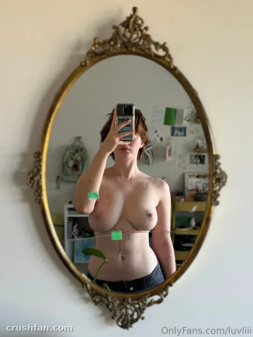 Lin prend un selfie miroir dans un miroir vintage à cadre doré, portant un jean et un harnais à chaînes dans une pièce lumineuse.