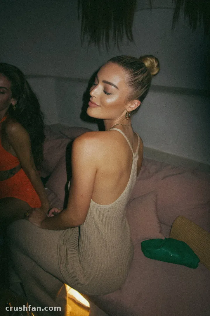 Nikki Rose in a beige ribbed dress sitting on a sofa in dim light