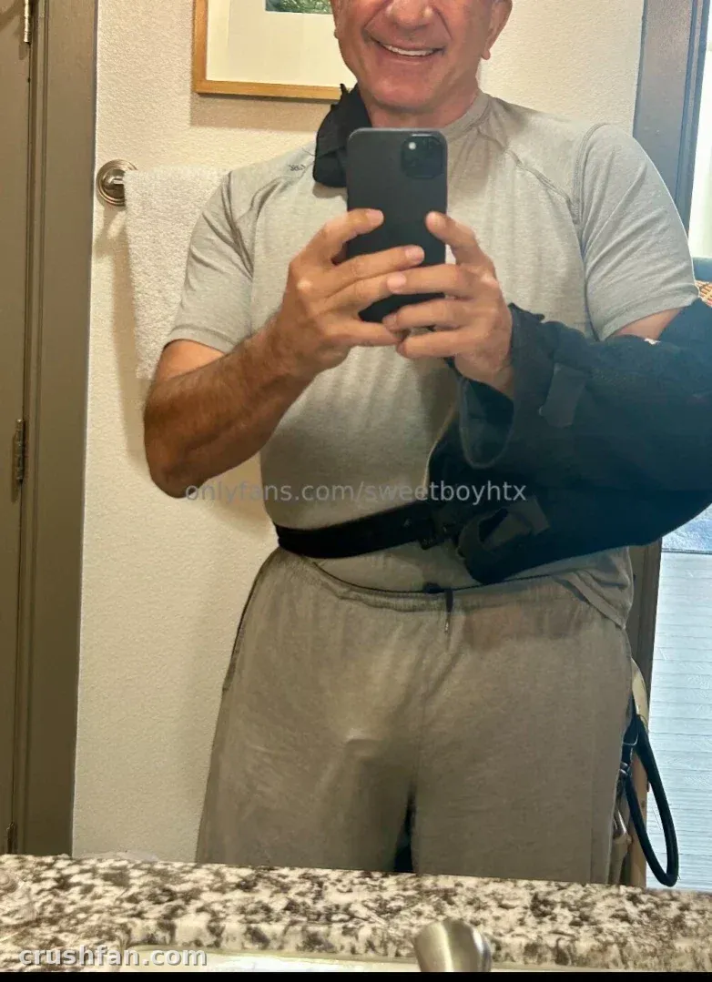 Sweet Boy nimmt ein Spiegel-Selfie in grauer Sportkleidung mit einer Armschlinge auf