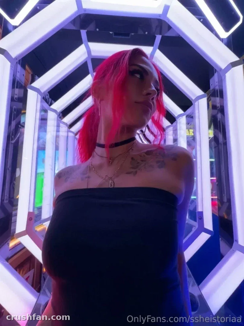 Femme aux cheveux roses en haut noir sans bretelles dans un tunnel de miroirs éclairé au néon
