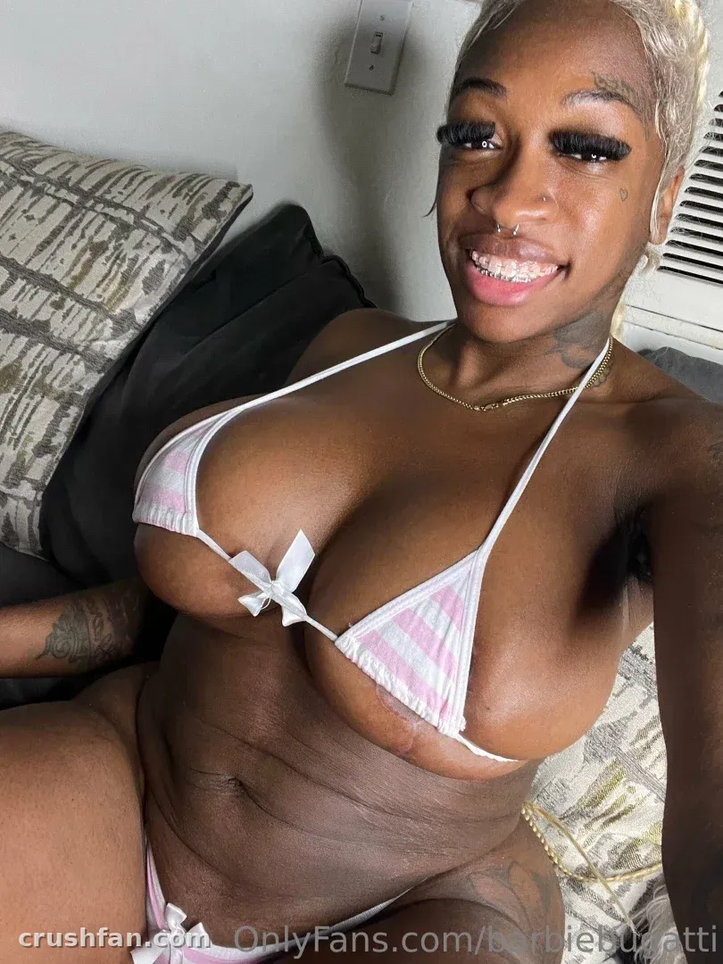 Barbie Bugatti smiling indoors in a pink and white bikini against dark cushions